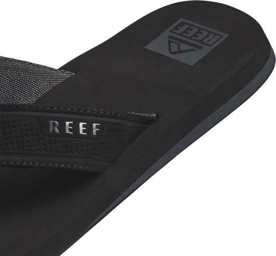 Detail van zwarte Reef slipper met stoffen band, Reef logo en zwarte zoolrand.