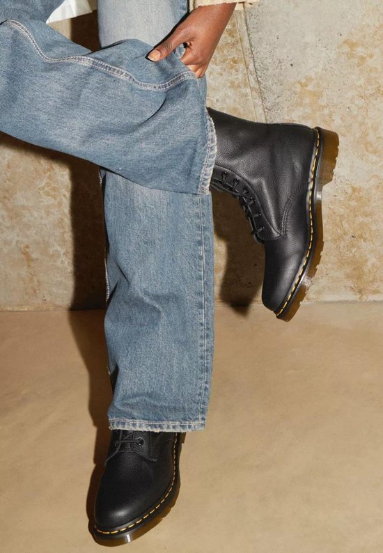 Une personne porte des bottes Dr. Martens noires avec un jean.