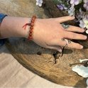 Een pols met een rode jaspis kralen armband met rood koord en houten detail. Zilveren ringen op de vingers.