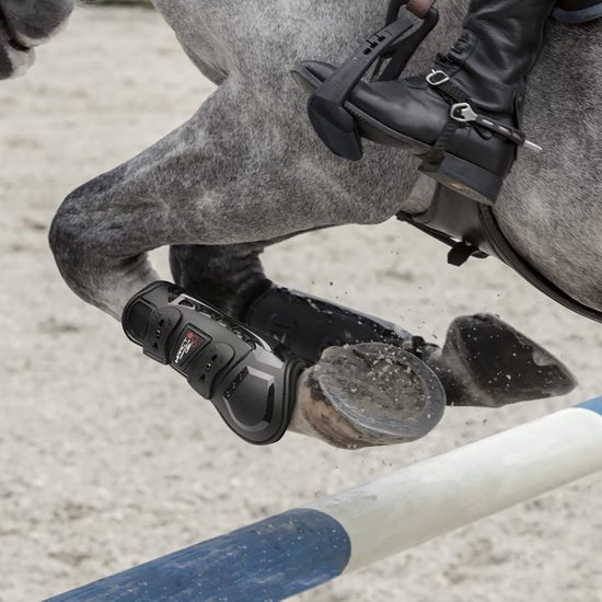 Grijze paardenbeen met zwarte peesbeschermers die over een hindernis springen.