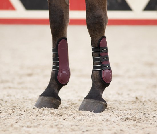 Twee donkerrode peesbeschermers om de voorbenen van een paard, met zwarte sluitingen.