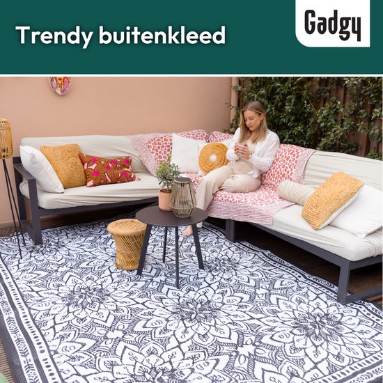 Tapis d'extérieur avec un grand motif mandala noir et blanc, sur une terrasse avec un canapé et des coussins.