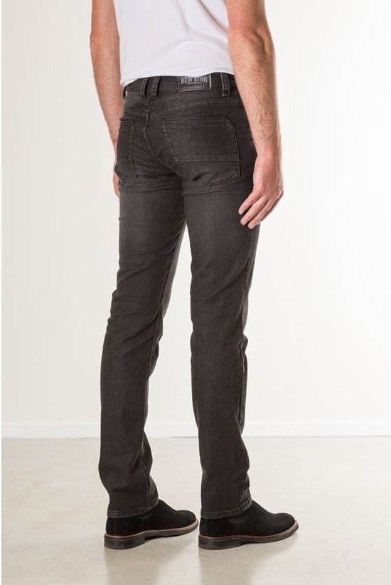 Zijaanzicht van een model in een zwarte, slim fit stretch spijkerbroek met bruine schoenen.