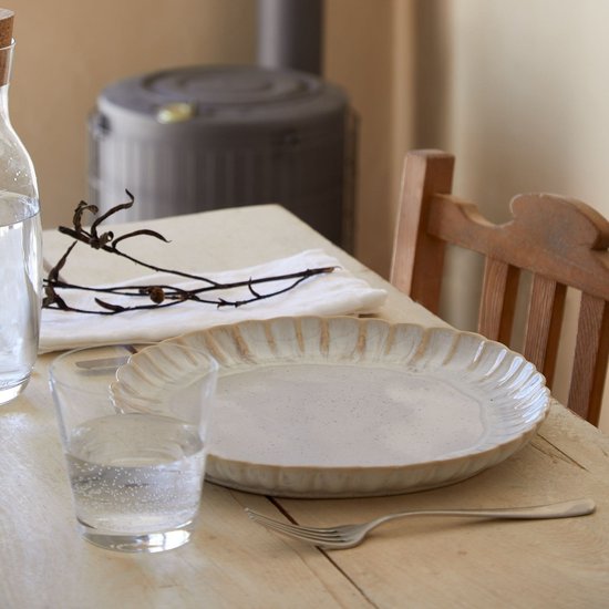 Crème keramisch dinerbord met geribbelde rand, op een houten tafel.