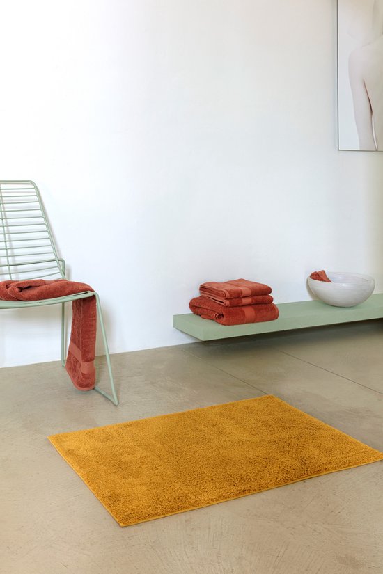 Okergele badmat in een minimalistische badkamer met oranje handdoeken.