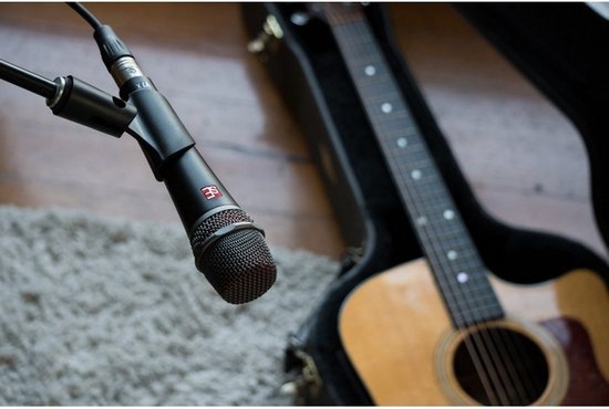 Zwarte sE microfoon met rood rooster, op een fluwelen tapijt, met een akoestische gitaar.