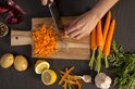 Bovenaanzicht: chef snijdt wortelen in blokjes op houten plank met Tefal mes. Citroenen, aardappelen, knoflook, ui, peperbolletjes erbij.