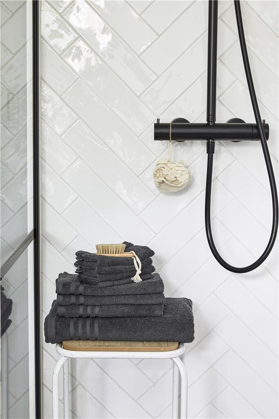 Serviettes anthracite sur un tabouret à côté d'une douche, avec une brosse et une éponge.