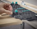 Hand met inbussleutel verstelt de groene knop op een grijze geleiderail met honingraatpatroon.