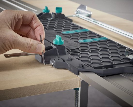 Hand met inbussleutel verstelt de groene knop op een grijze geleiderail met honingraatpatroon.