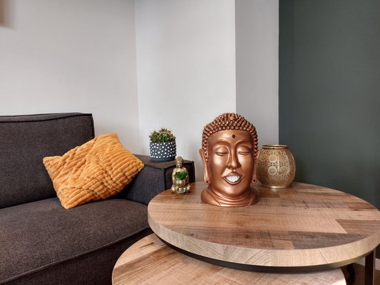 Bronzen Boeddha hoofd tissuehouder op een salontafel naast sierobjecten.