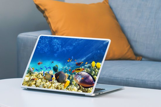 Ordinateur portable avec autocollant monde sous-marin : coraux, poissons et poisson-lion, sur une table à côté d'un canapé.