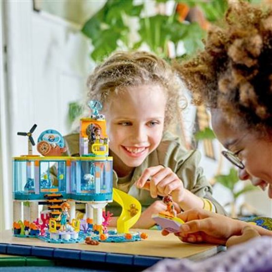 Twee kinderen spelen met een LEGO Friends speelset van een zee reddingscentrum, met speelgoed figuren en dieren.