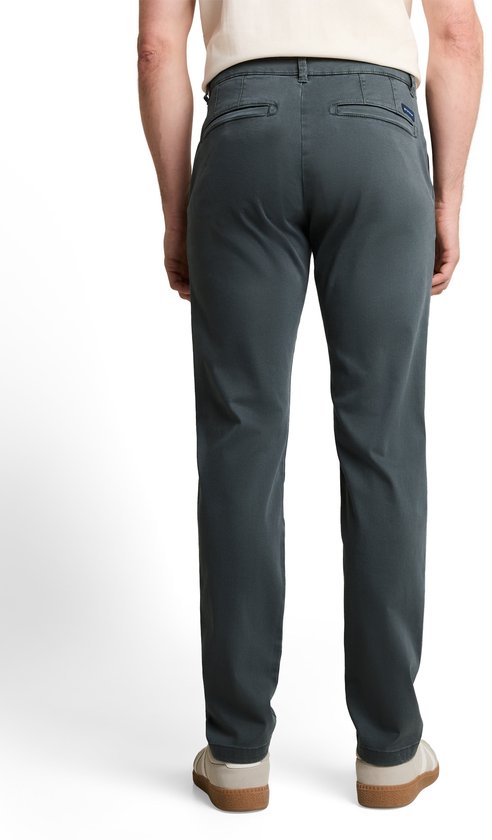 Model draagt een donkergrijze slim-fit chino, beige T-shirt en lichte sneakers, achterkant.