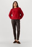 Model draagt een bruine leren broek en een rode gebreide trui.