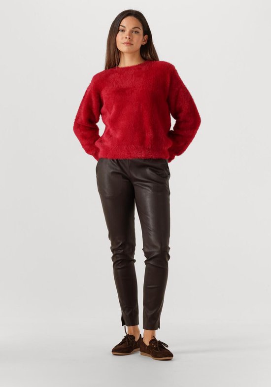 Model draagt een bruine leren broek en een rode gebreide trui.