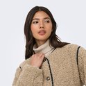 Model van rechts, draagt een beige teddy jas met zwarte bies en coltrui. Houdt de kraag vast.