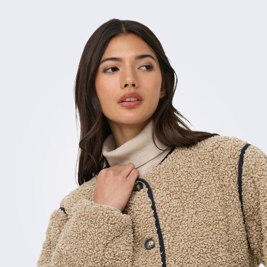 Model van rechts, draagt een beige teddy jas met zwarte bies en coltrui. Houdt de kraag vast.