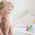 Meisje met krullen kijkt naar roze schaap wekker met groene verlichting.