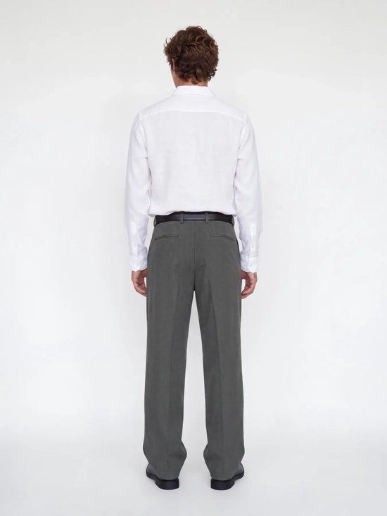 Man met donker haar, rug zichtbaar, draagt grijze pantalon met wijde pijpen en witte blouse.