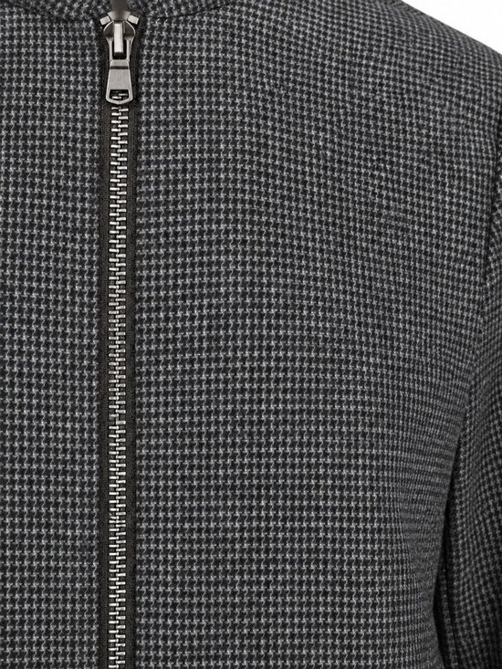 Close-up van de textuur van het donkerblauwe jack met pepita-motief en ritssluiting.