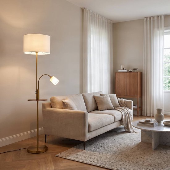 Messing vloerlamp met wit stoffen kap, leeslamp en klein houten bijzettafeltje in een modern interieur.