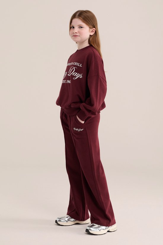 Meisje in een bordeauxrode joggingbroek en sweater met 'Cozy Days' print. EST. 1961.