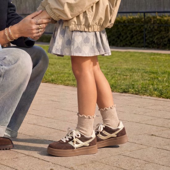 Bruine Posh sneakers met plateauzool, witte accenten en veters met kraaltjes, gedragen onder een rokje met hartjes.