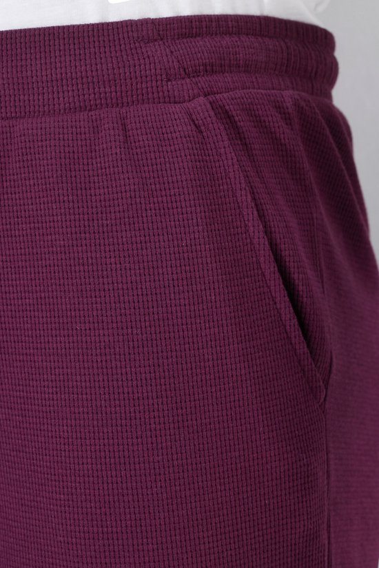 Zakdetail op een donkerpaarse sweatculotte met wafelstructuur.
