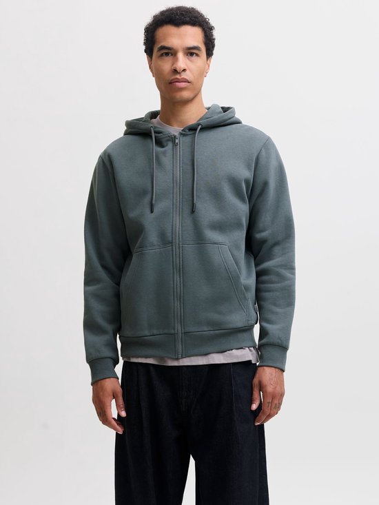 Model draagt een effen, donkergroene hoodie met ritssluiting en capuchon.
