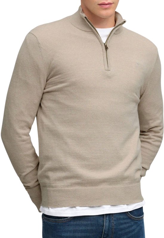 Man in beige trui met halve rits, witte t-shirt en blauwe jeans.