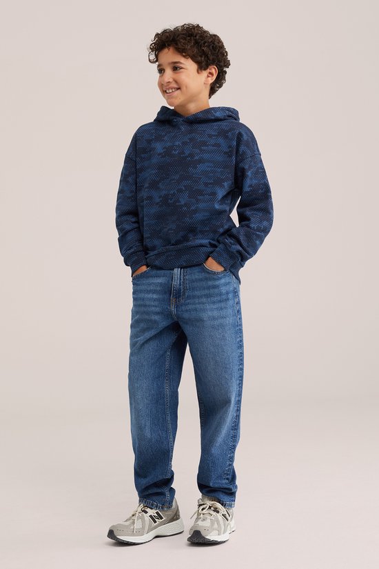 Jongen draagt een marineblauwe hoodie met zeshoekig patroon, gecombineerd met een blauwe jeans en sneakers.