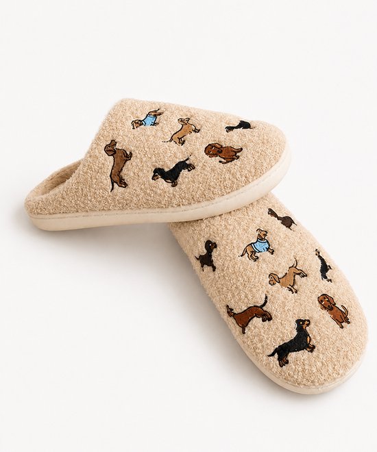 Paar beige, pluizige pantoffels met geborduurde teckels in verschillende stijlen en kleuren.
