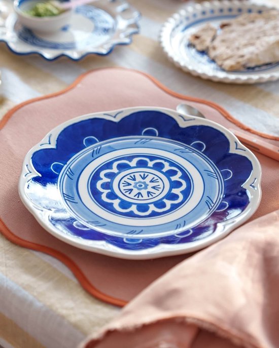 Porseleinen bord met golvende rand en blauw-wit Majolica patroon op een perzikkleurige placemat.