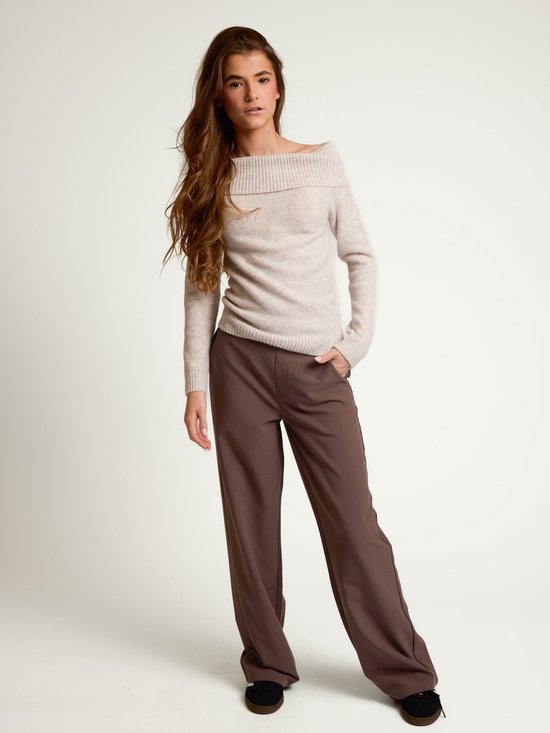 Model in een lichtbruine off-shoulder coltrui en bruine wijde broek.