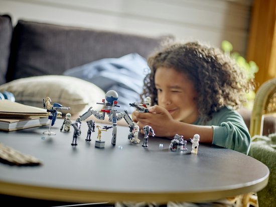 Een jongen speelt met LEGO Star Wars-figuren, waaronder clone troopers, battle droids, een speeder en een tri-droid.