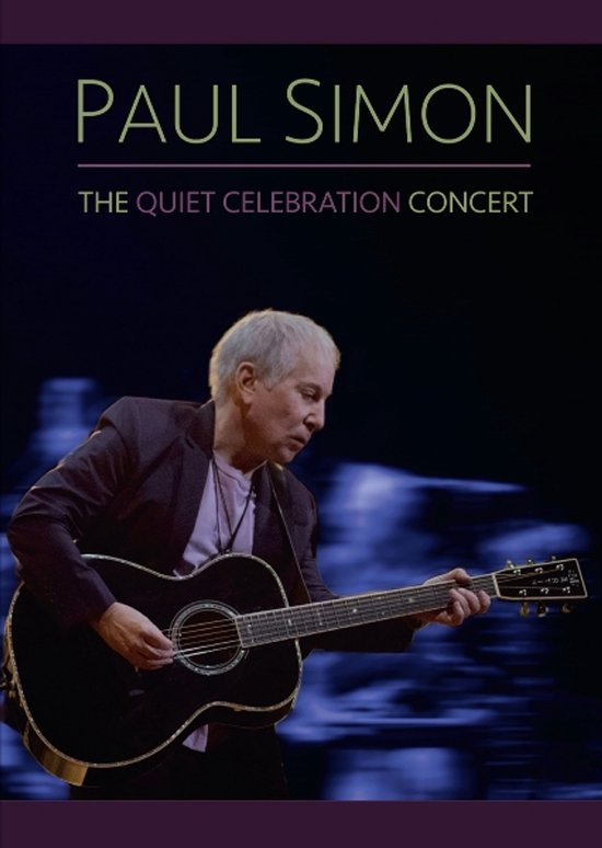 Paul Simon speelt akoestische gitaar tijdens The Quiet Celebration Concert tegen een donkere achtergrond.