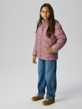 Model draagt een roze gewatteerde jas, blauwe jeans en bruine sneakers.