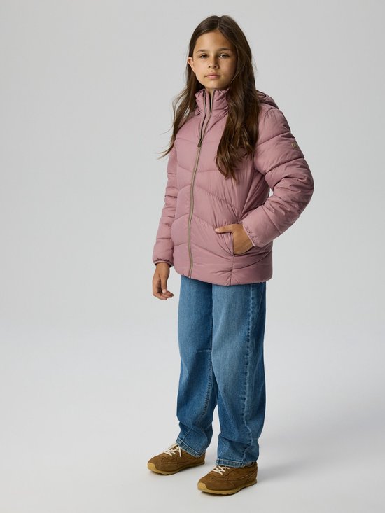 Model draagt een roze gewatteerde jas, blauwe jeans en bruine sneakers.