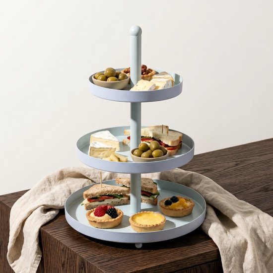 Lichtblauwe etagère op een houten tafel, gevuld met olijven, kaas, sandwiches en diverse kleine taartjes.