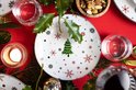 Feestelijk gedekt wit bord met kerstdecoratie, midden op een rode tafelkleed omringd door hulst.