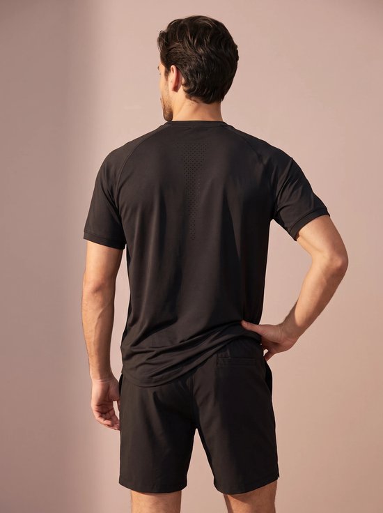Man draagt zwart sportshirt met perforaties op de rug en zwarte sportshort.