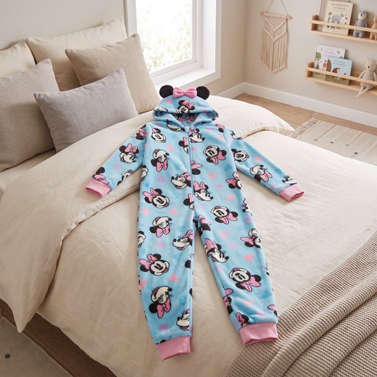 Blauwe Minnie Mouse fleece onesie met roze hartjespatroon, liggend op een beige bed.