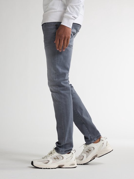 Model draagt een grijze slim fit jeans van Petrol Industries met vintage wassing en beige sneakers.