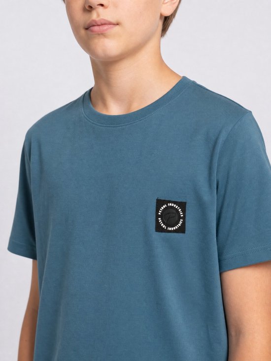 Jongen draagt een blauw katoenen T-shirt met korte mouwen en een zwart logo op de borst.