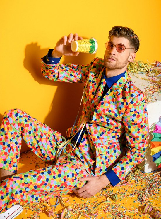 Man met zonnebril en confettibeker in veelkleurig pak met confettiprint, zittend.