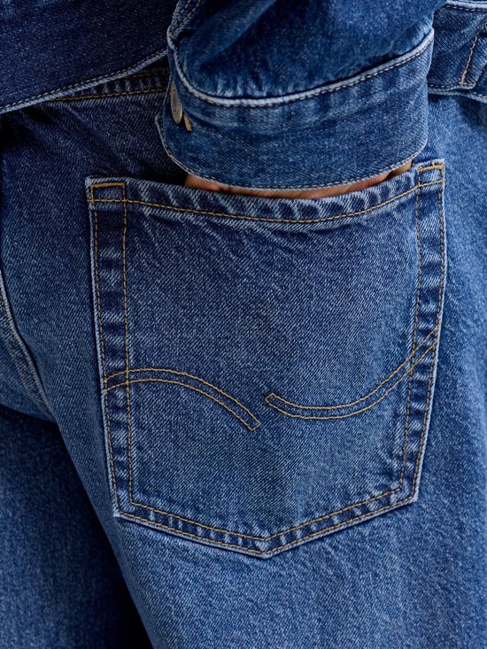 Donkerblauwe jeans achterzak met gele sierstiksels en een ingestopte hand.