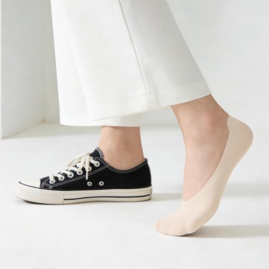 Voet met beige onzichtbare sok naast een zwarte sneaker.