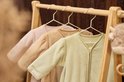 Drie baby slaapzakken in pastelkleuren: lichtroze, beige en mintgroen, hangend aan een houten rek.