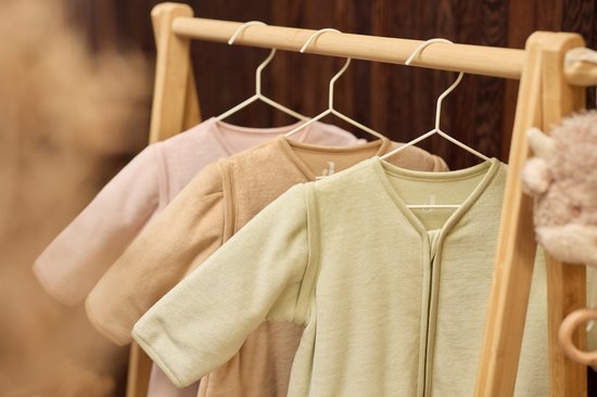 Drie baby slaapzakken in pastelkleuren: lichtroze, beige en mintgroen, hangend aan een houten rek.